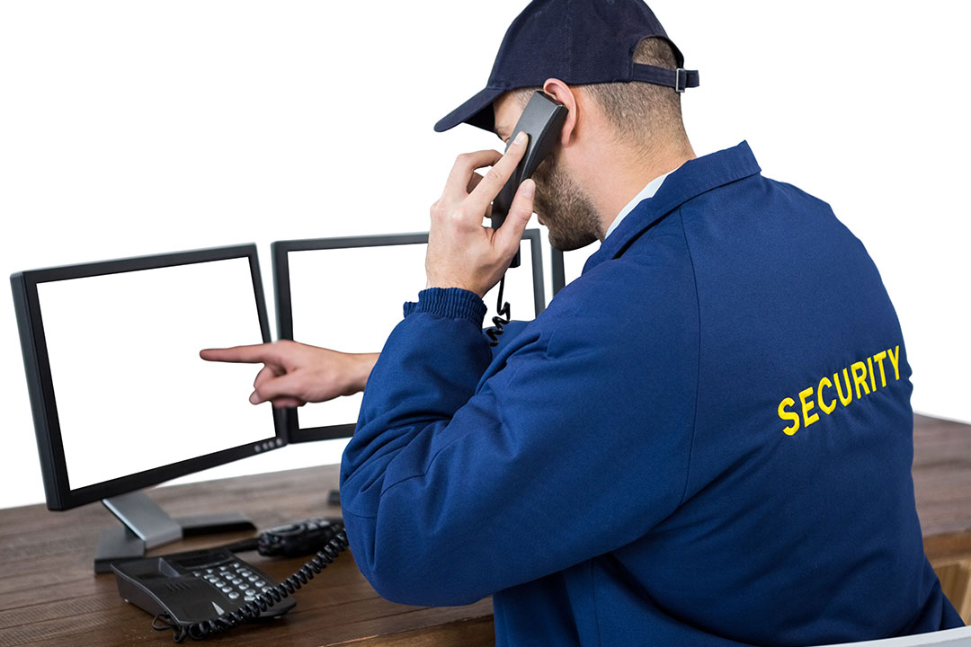 Security officer talking on phone while pointing at computer monitors